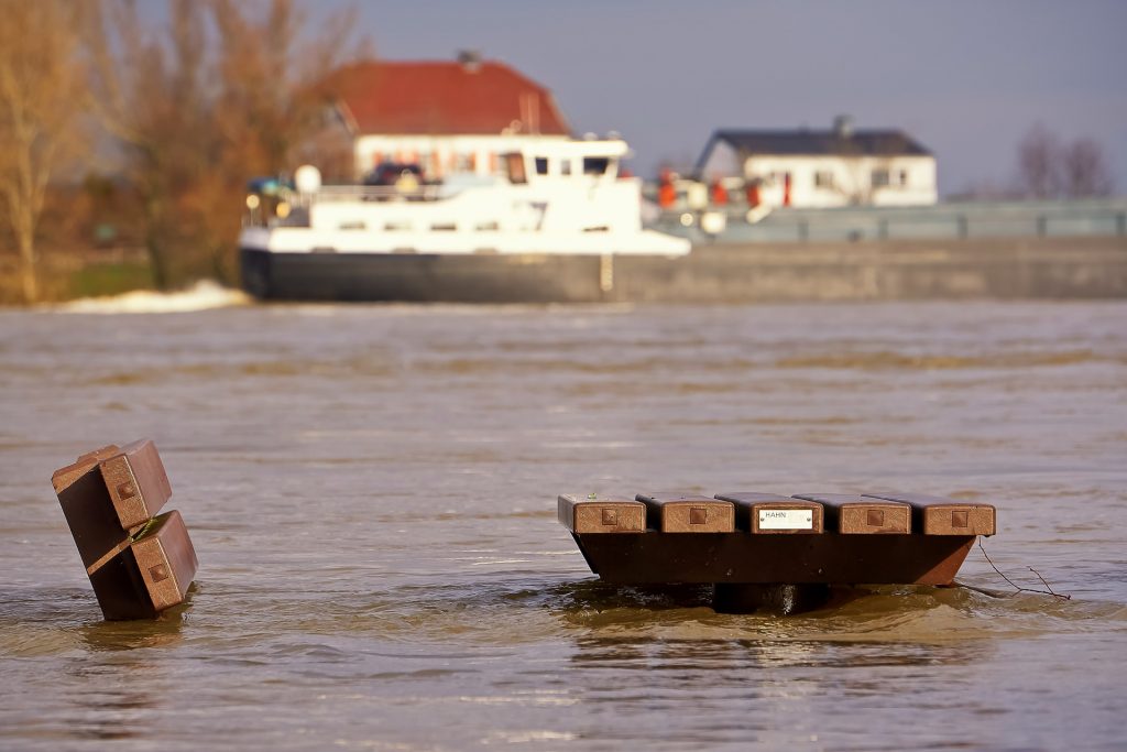 Overstroomd bankje met binnenvaartschip op de achtergrond